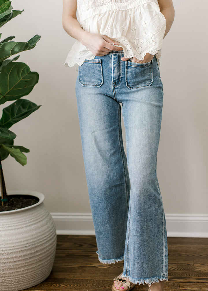 Model wearing a medium/light wash ankle jeans with high rise, wide leg fit with a frayed hem.