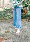 Model wearing heels with medium wash jeans with a cropped wide leg fit and floral at hem. 