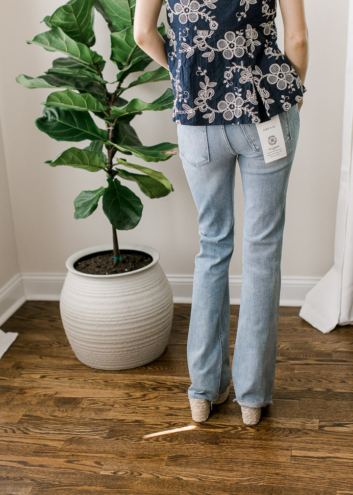 Back view of Model wearing medium/light wash jeans with  high rise bootcut fit and a raw hemline. 