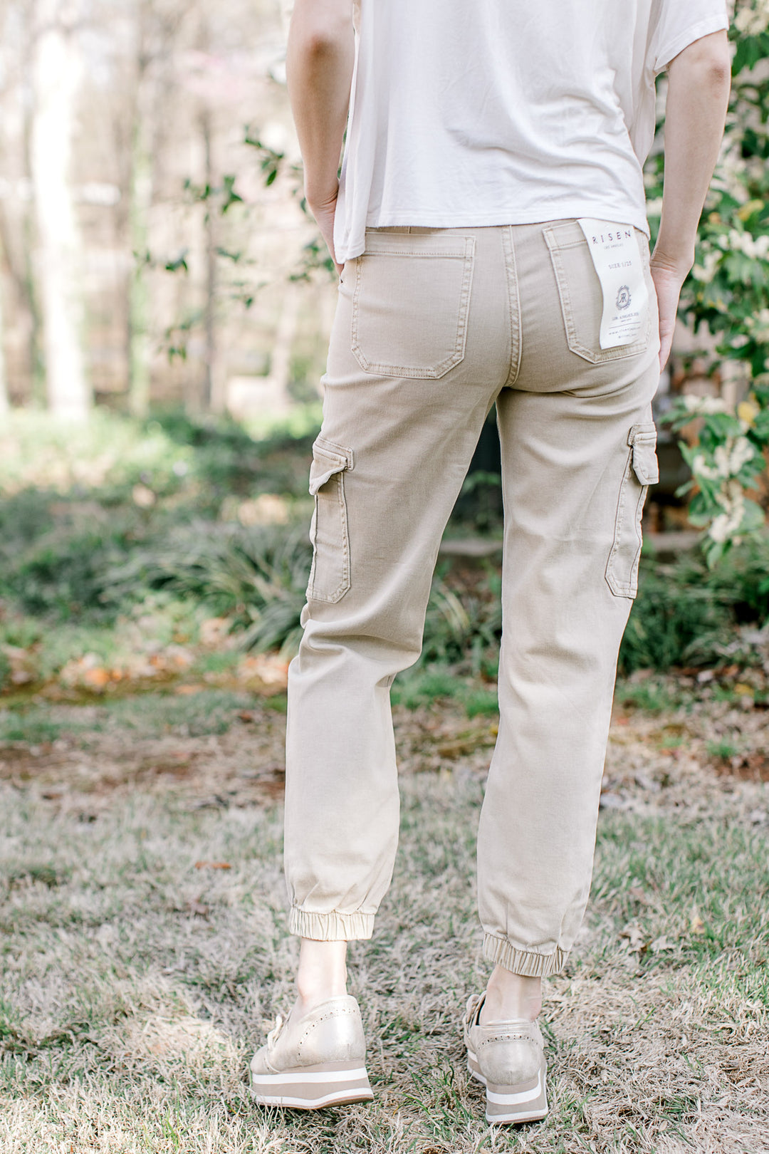 Back view of Model wearing Risen brand cargo joggers with a soft taupe color. 