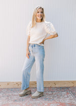 Model wearing a cream sweater with light wash jeans with wide legs and a high waist. 