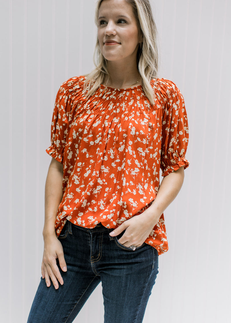 Model wearing a rust top with cream floral, keyhole closure, detail at neck and bubble short sleeves