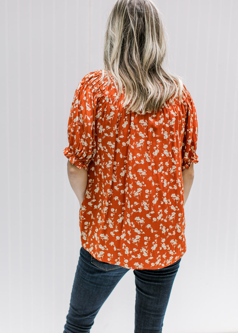 Back view of Model wearing a rust top with cream floral, detail at neck and bubble short sleeves.