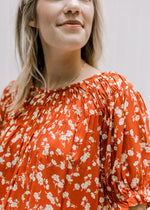 Close up view of bubble short sleeves and detail at the neck of a rust top with cream floral. 