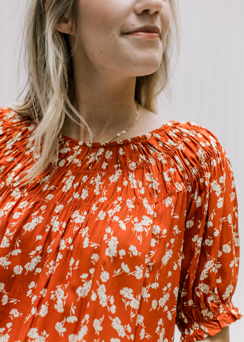 Close up of bubble short sleeves, round neck detail and rust top with a cream floral detail. 