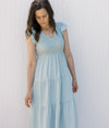 Model wearing a light blue tiered midi with a smocked bodice, v-neck and flutter capped sleeves. 