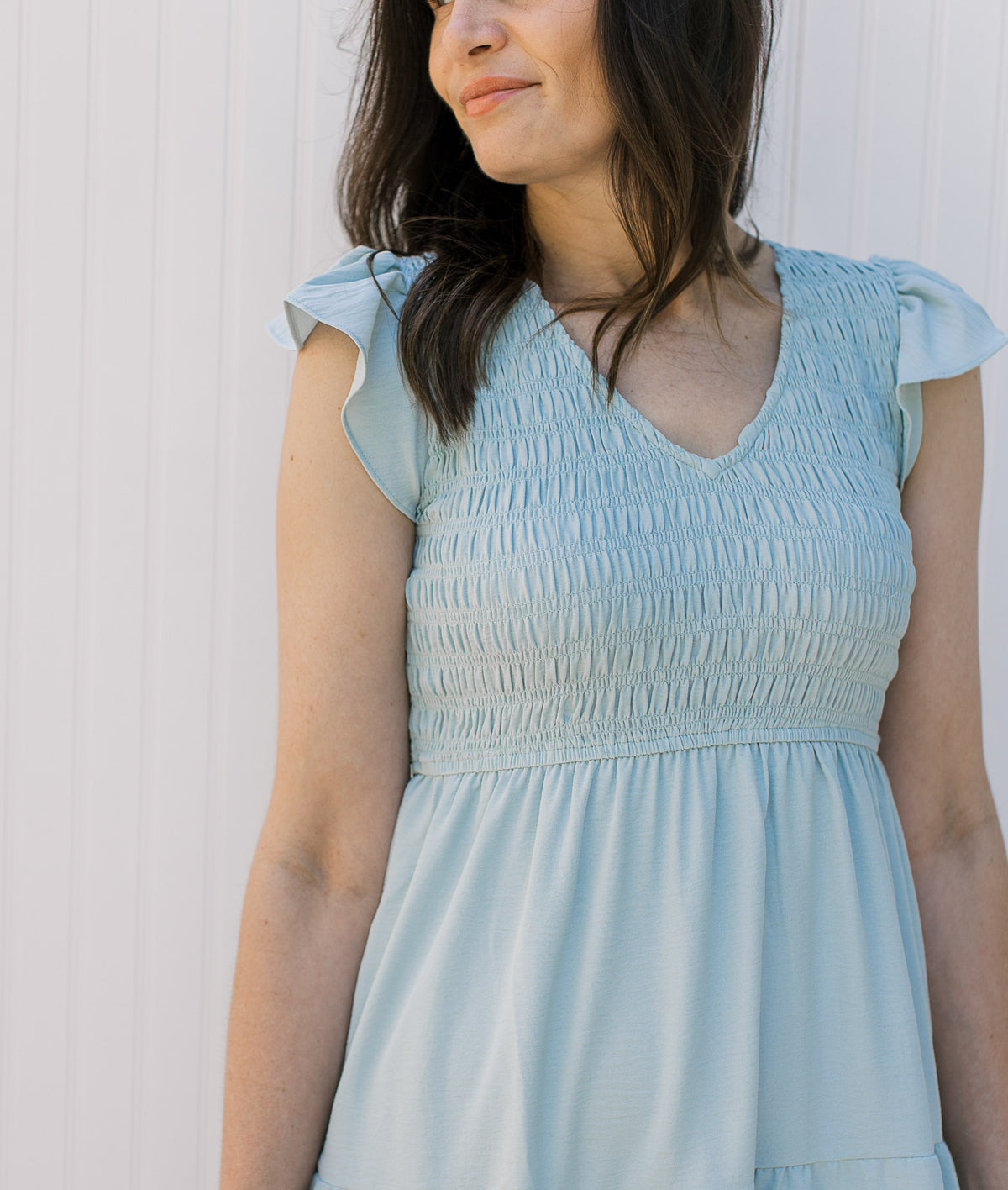 Close up of smocked bodice, v-neck and ruffle capped sleeves on a tiered light blue midi. 