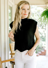 Model wearing a black sweater with capped sleeves, mock neck and cream scalloped hem.