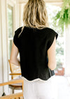 Back view of Model wearing a black ribbed sweater with capped sleeves and cream scalloped hem.
