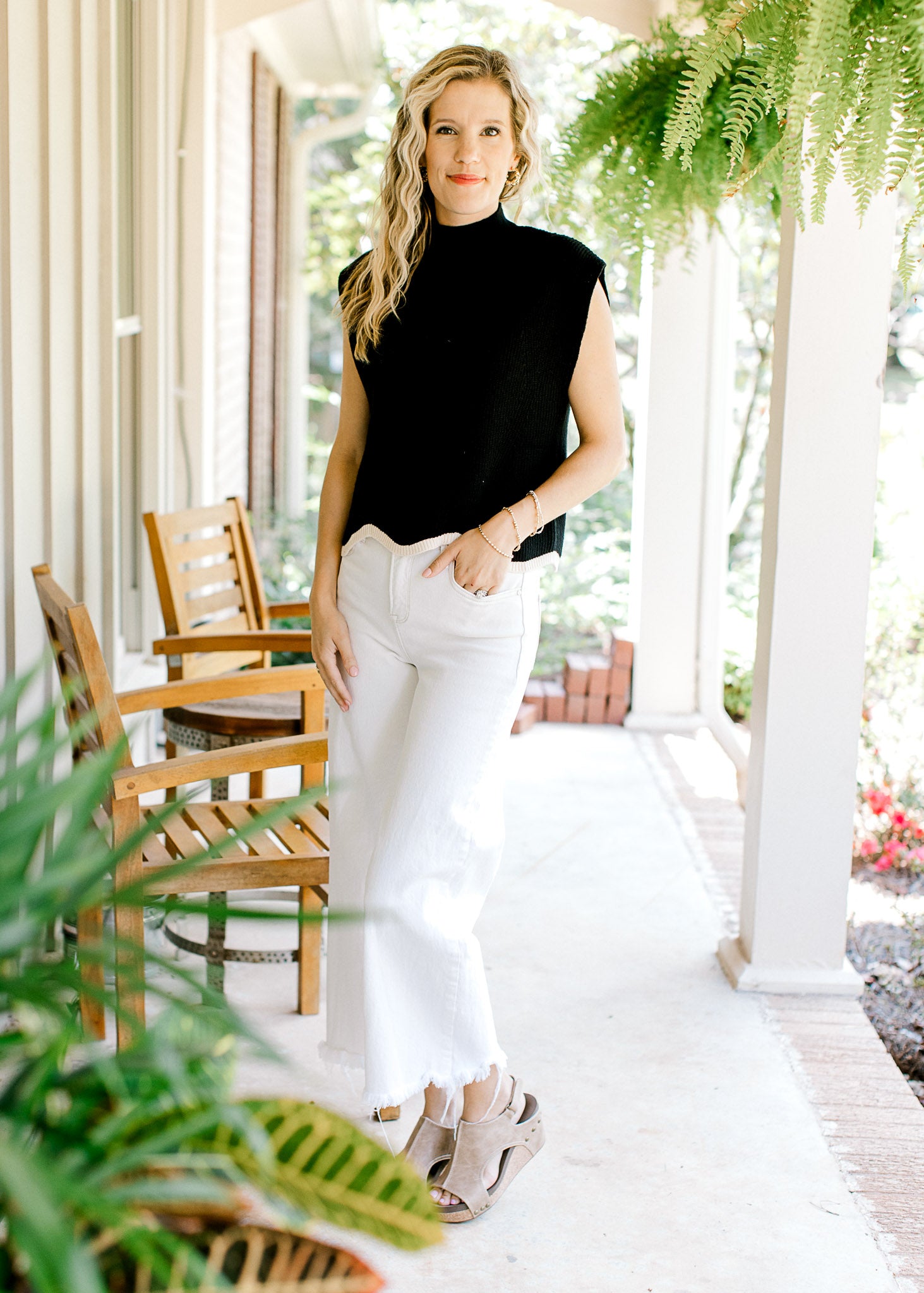 Model wearing white pants with a black sweater with capped sleeves and cream hem.