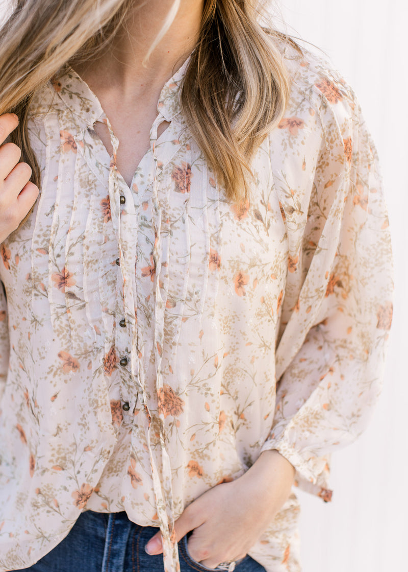 Close up of micro pleating, bronze buttons and tie at the v-neck of a cream top with russet and green floral.
