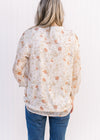 Back view of Model wearing a cream top with russet and green floral v-neck top with 3/4 sheer sleeves.