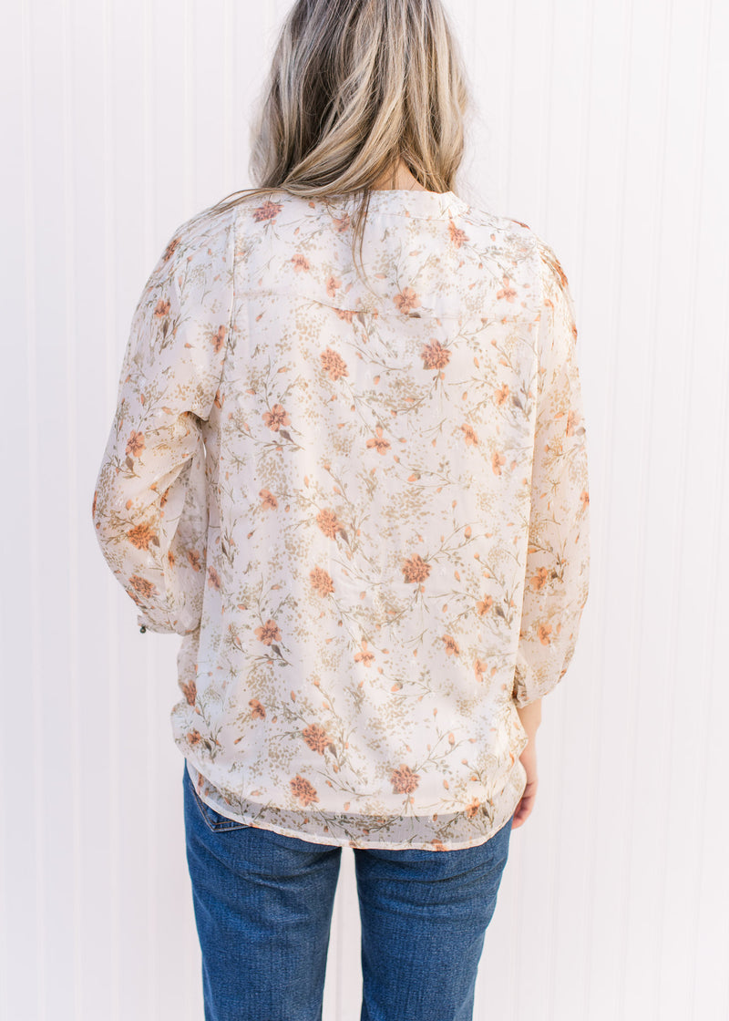 Back view of Model wearing a cream top with russet and green floral v-neck top with 3/4 sheer sleeves.