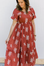 Model wearing a rust maxi with white embroidered flower sprigs, short sleeves and a square neck.