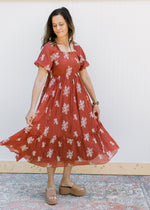 Model wearing a rust maxi with white embroidered flower, puff short sleeves and a square neck.