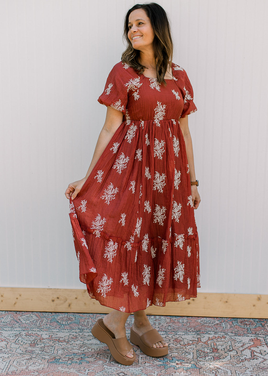 Model wearing a rust dress with white embroidered flower sprigs, short sleeves and a square neck.