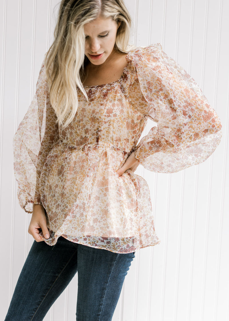 Model wearing a beige top with a rust floral pattern, sheer long sleeves and a square neckline.