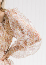 Close up of sheer long sleeve and ruffle at neck on a white top with rust floral pattern.