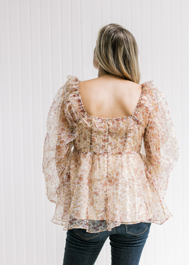Back view of Model wearing a beige top with a rust floral pattern, a square neck and zip closure. 