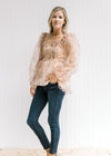 Model wearing jeans, wedges and a beige top with a rust floral pattern and sheer long sleeves. 