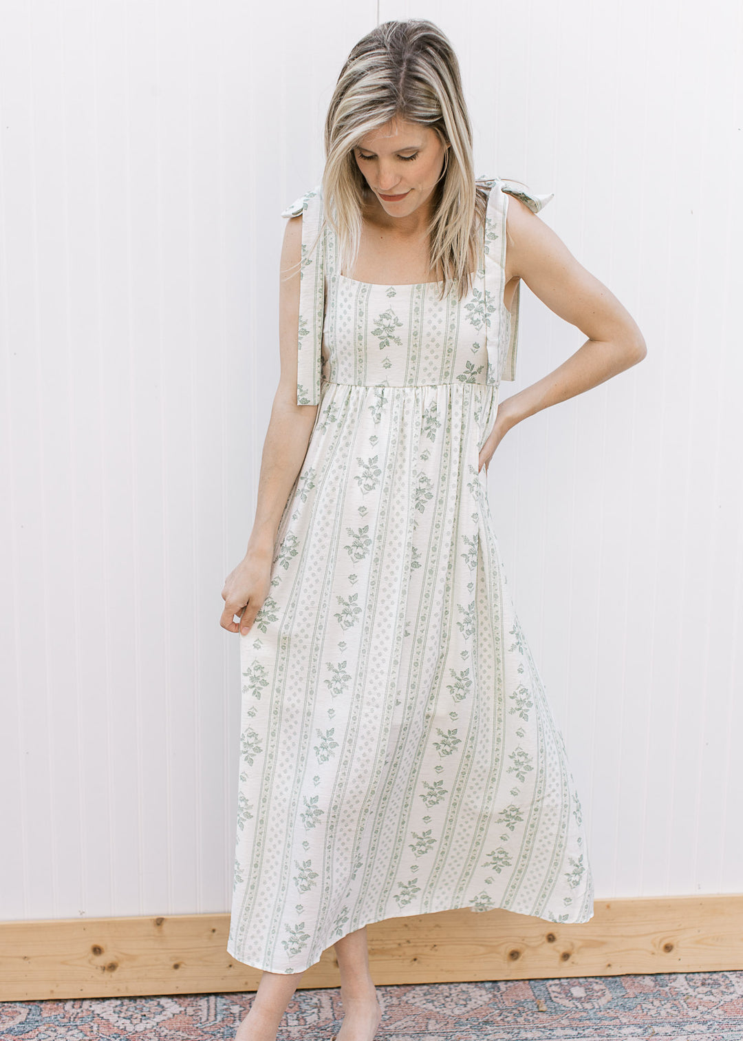 Model wearing a cream midi with sage floral, square neck, adjustable tie straps and smocked back.
