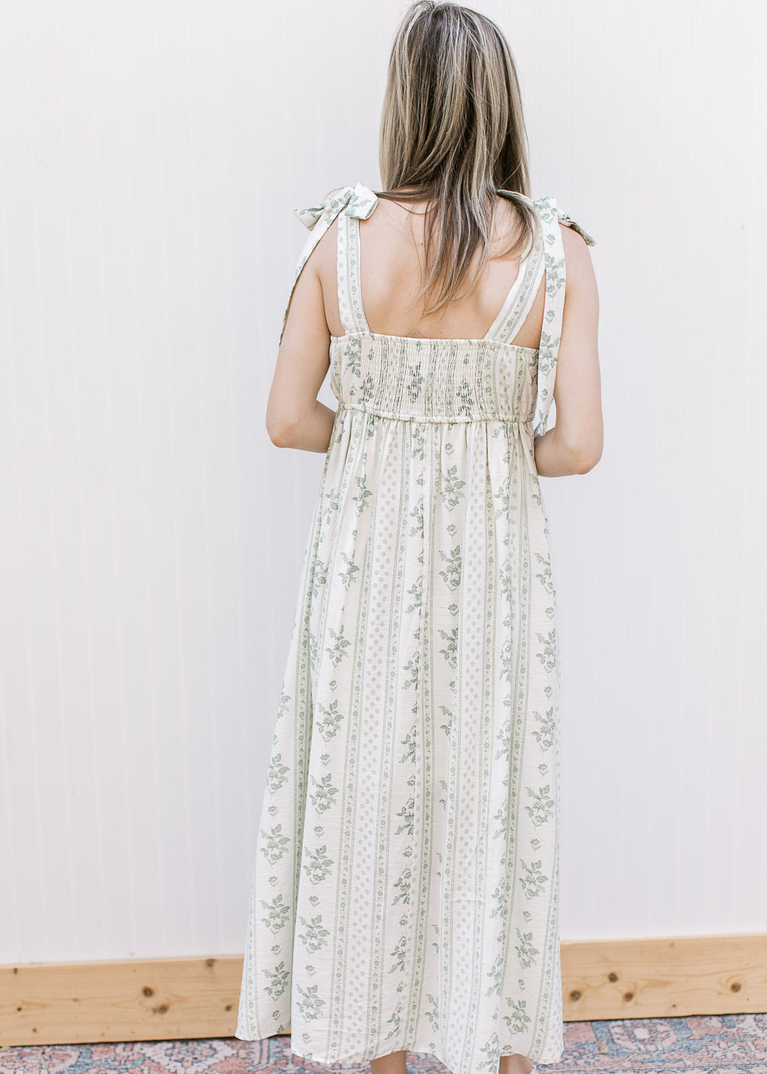 Back view of Model wearing a cream midi with sage floral, adjustable tie straps and smocked back.