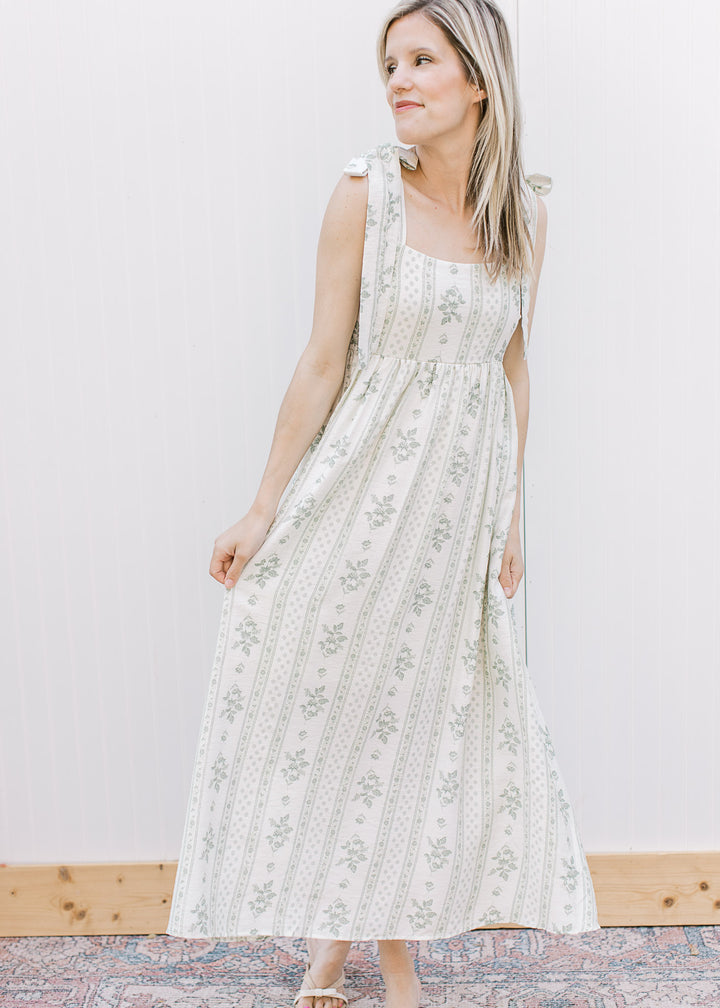 Model wearing a flowy cream midi with sage floral, square neck, tie straps and smocked back.