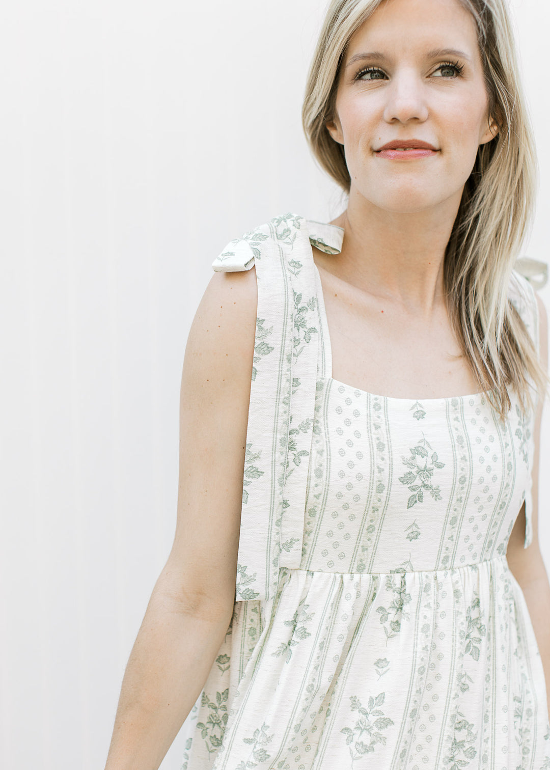Close up of tie strap and square neckline on a cream midi dress with sage floral pattern. 