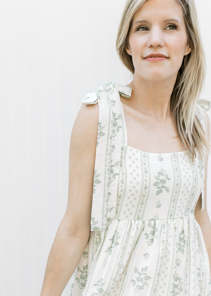 Close up of tie strap and square neckline on a cream midi dress with sage floral pattern. 
