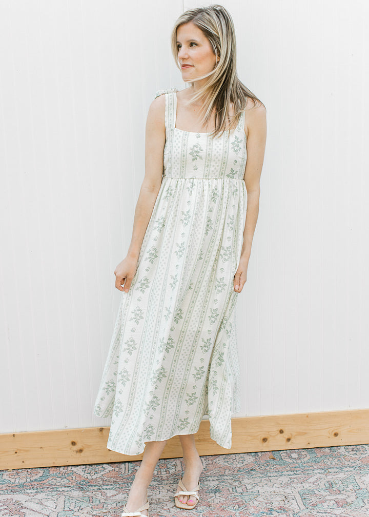 Model wearing heels and  a cream midi with sage floral, square neck, tie straps and smocked back.