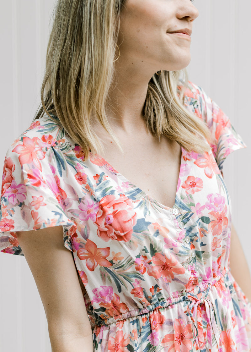 Close up view of model wearing a v-neck dress with cream background and pink floral pattern. 