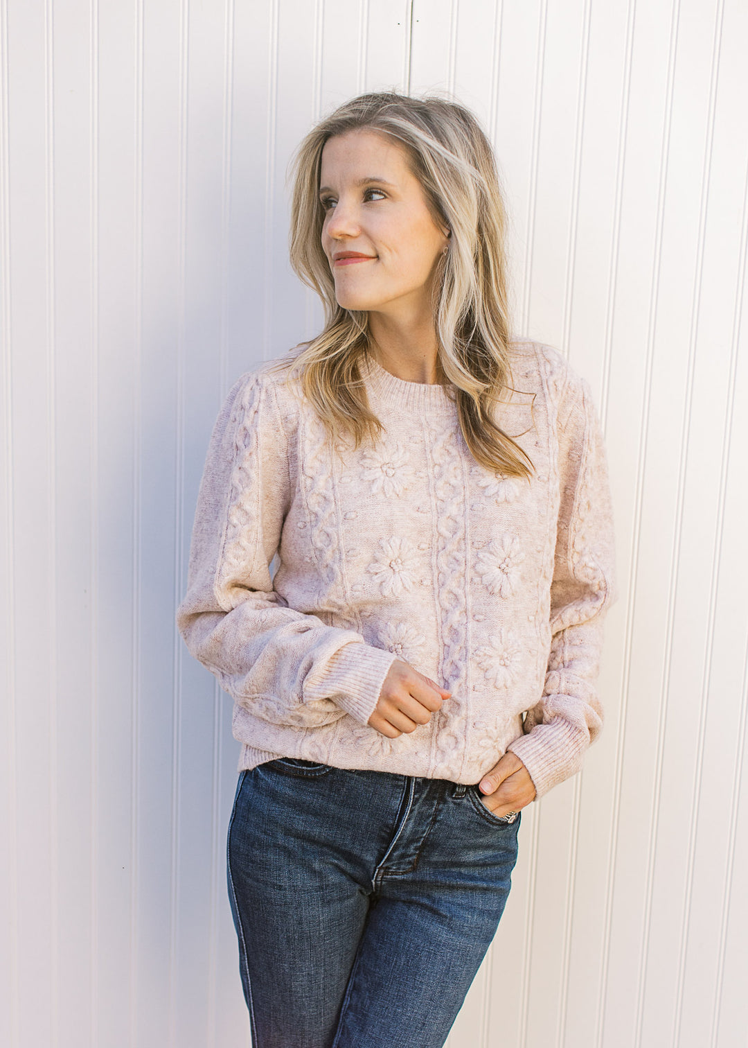 Model wearing a cream sweater with embossed design, long sleeves and a round neckline.