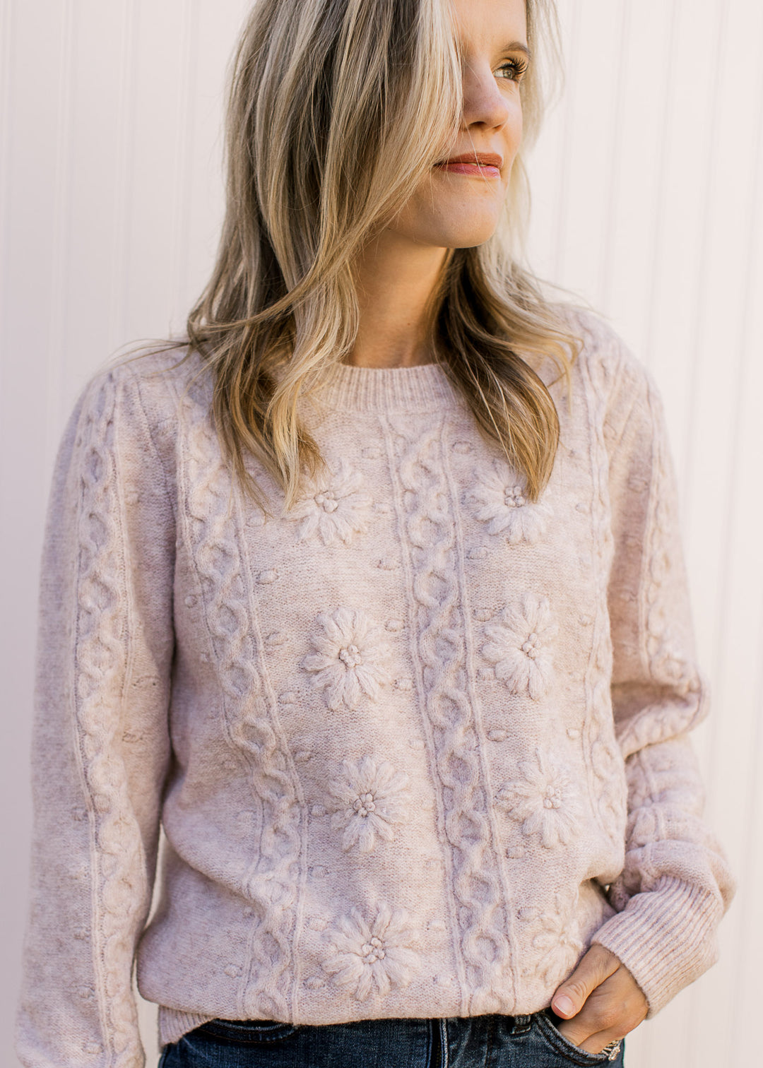 Model wearing a cream sweater with embossed design, long sleeves and a round neck.
