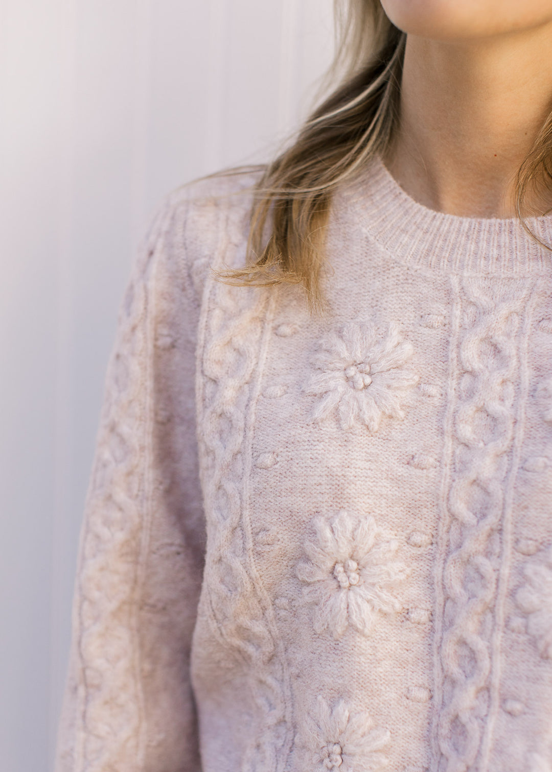 Close up of flower and geometric design on a cream sweater with long sleeves and a round neck.