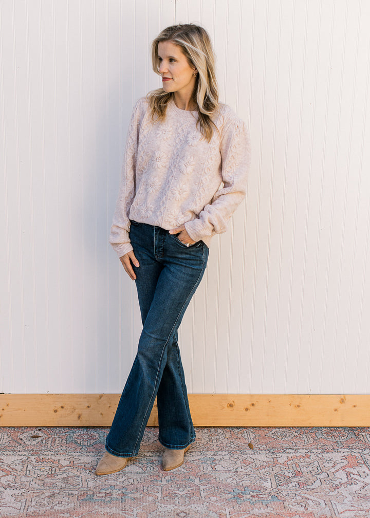 Model wearing jeans and a cream sweater with embossed design, long sleeves and a round neckline.
