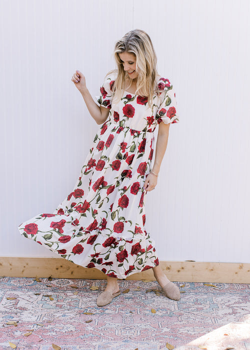 Model wearing a cream maxi with red roses, square neck and bubble short sleeves. 