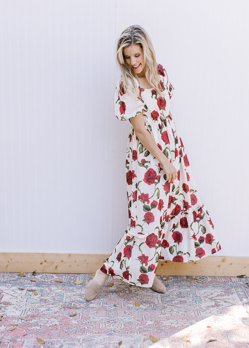 Model spinning in a cream maxi with red roses, square neck and bubble short sleeves. 