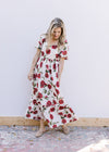 Model wearing a cream flowy dress with red roses, square neck and bubble short sleeves. 