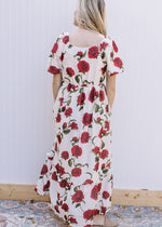 Back view of Model wearing a cream maxi with red roses, square neck and bubble short sleeves. 