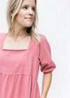 Close up of square neckline and bubble short sleeves on a rose colored above the knee dress. 
