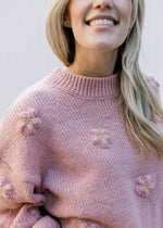 Close up of mock neck and 3D flowers on a rose colored knit sweater with long sleeves. 