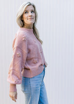 Side view of Model wearing a rose colored sweater with a mock neck, 3D flowers and long sleeves. 