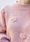 Close up of 3D flower and knit material on a rose colored sweater with long bubble sleeves. 