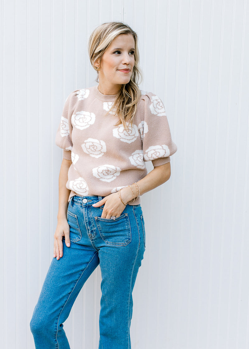 Model wearing jeans with a soft pink sweater with cream roses and bubble short sleeves.