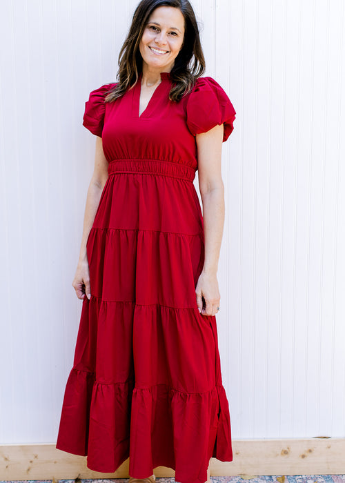 Model wearing a red midi with elastic band at waist, tiered skirt and short puff sleeves. 