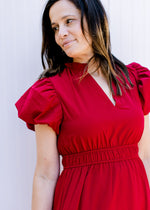 Close up of v-neck, short puff sleeves and elastic waist on a red midi with a tiered skirt.