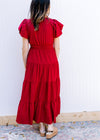 Back view of Model wearing a red midi with elastic waist, tiered skirt and short puff sleeves. 