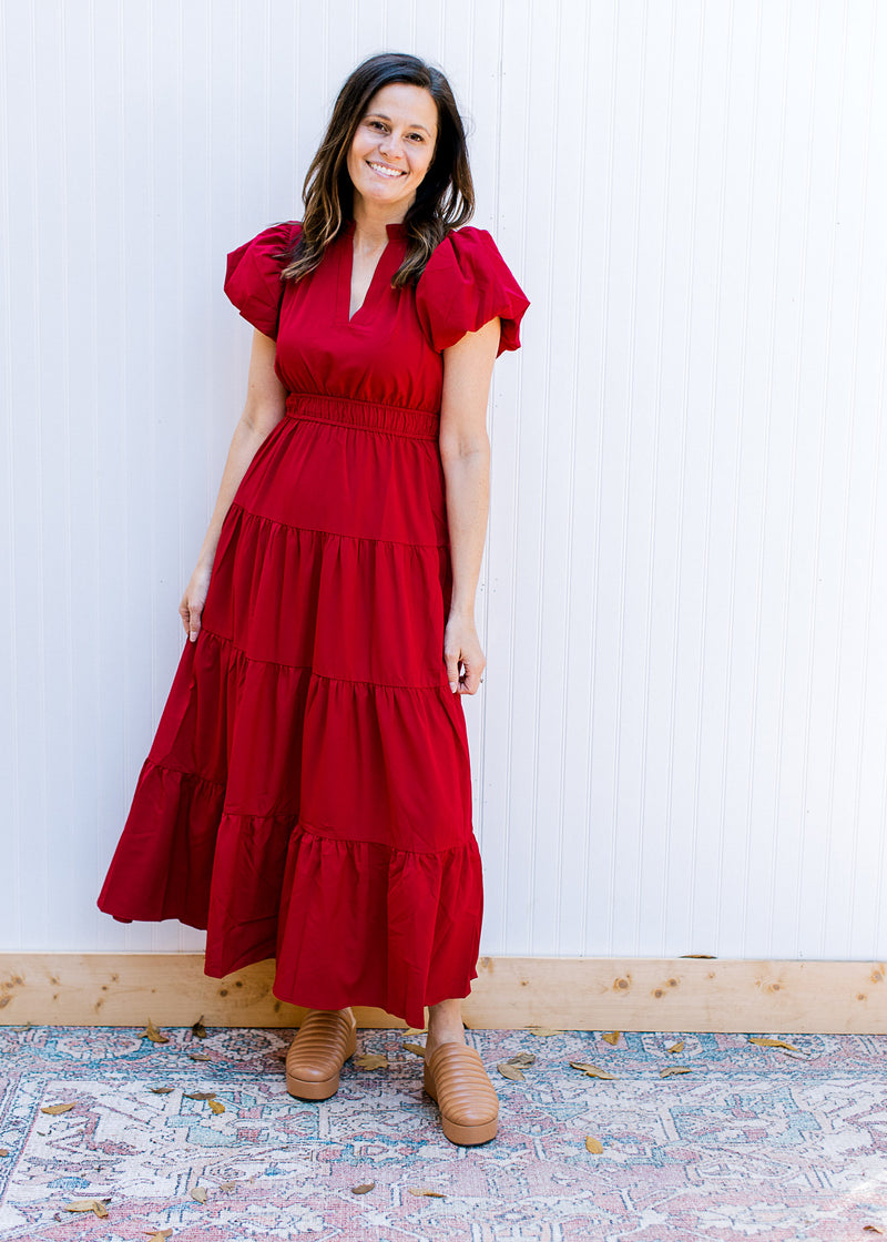 Model wearing clogs and a red dress with elastic waist, tiered skirt and short puff sleeves. 