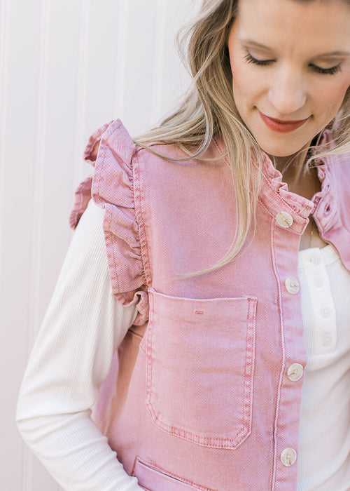 Model wearing a mauve denim vest with ruffle at arm and neck, button front and patch pockets.