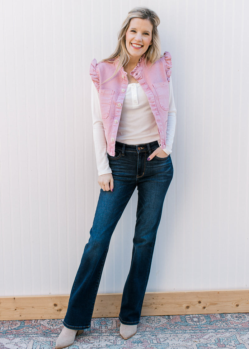 Model wearing jeans, white top and a mauve denim vest with ruffle at arm and neck. 